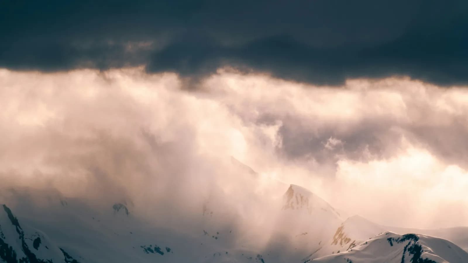 Snow-covered mountains beneath dramatic sunlit clouds